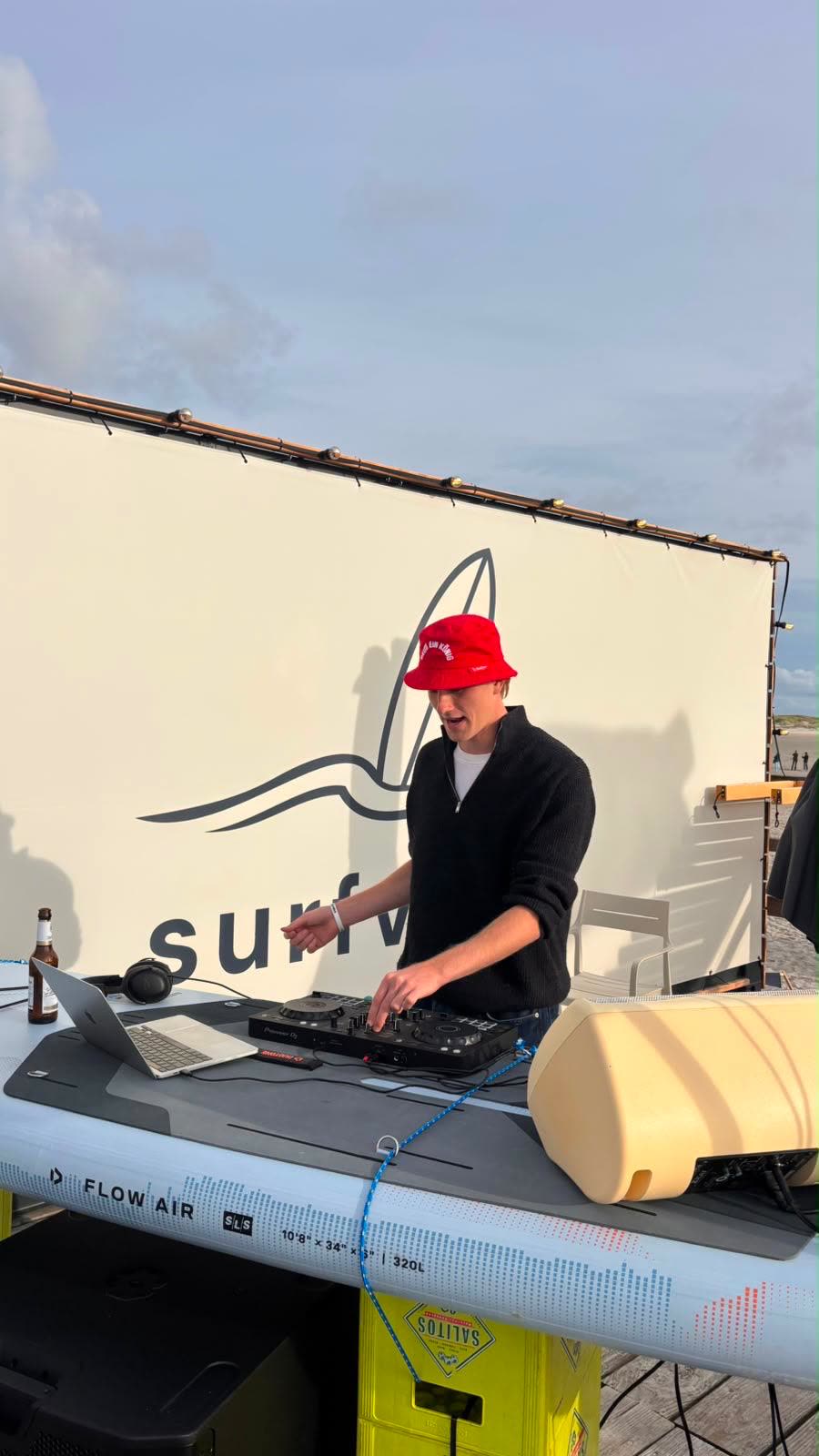 Hendrik Wulf DJing outdoors at a beach event, wearing a red bucket hat